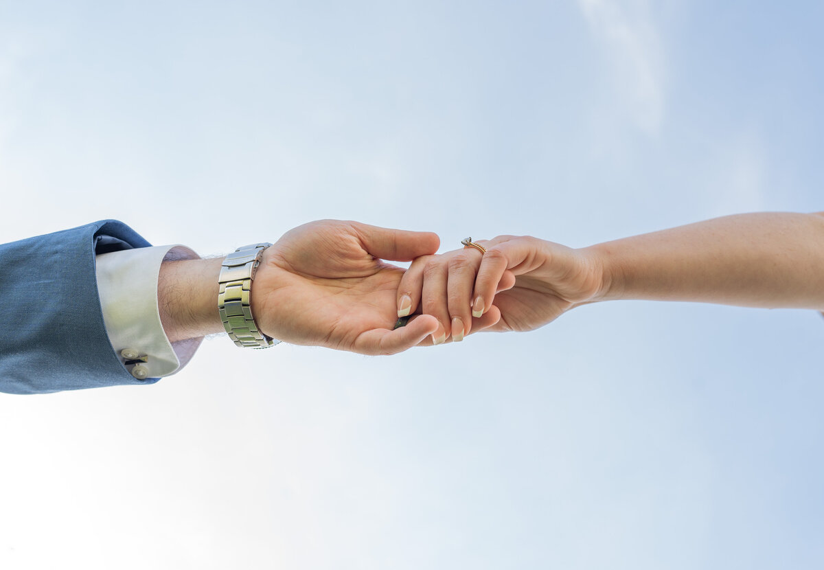 Bride and Groom holding hands with the sky as the background. The  brides big diamond ring is shining.