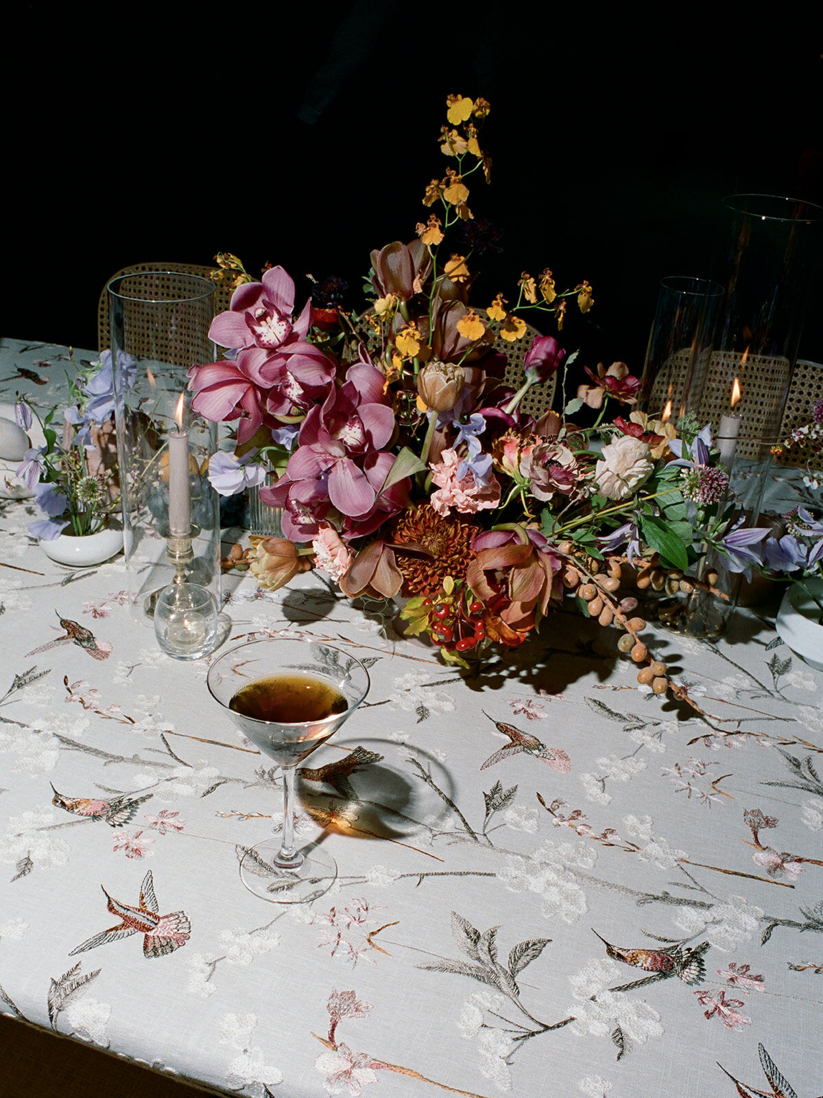 Clustered and styled floral arrangements, fruits, and art pieces for fall wedding reception. Low centerpieces mixed with ikebana arrangements and bud vases decorate the reception tables at this fall wedding. Floral centerpieces featuring orchids, ranunculus, sweet peas, and bittersweet. Styled wedding tables with fruits, curated candles, and floral arrangements. Tasteful fall color palette of copper, ruby, gold, burgundy, rust, and lavender. Design by Rosemary & Finch Floral Design in Nashville, TN.