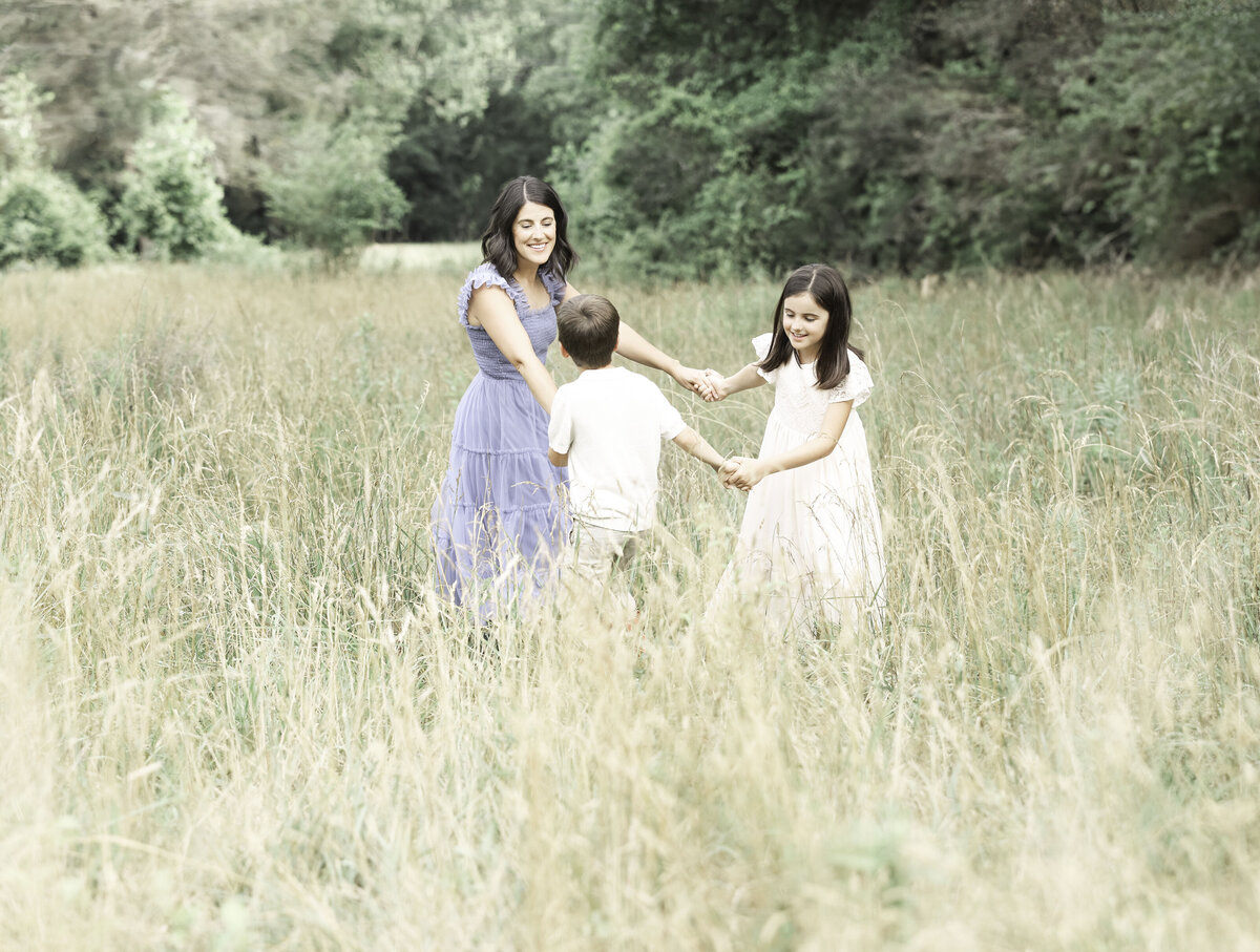 two children and their mother play ring around the rosy in a field
