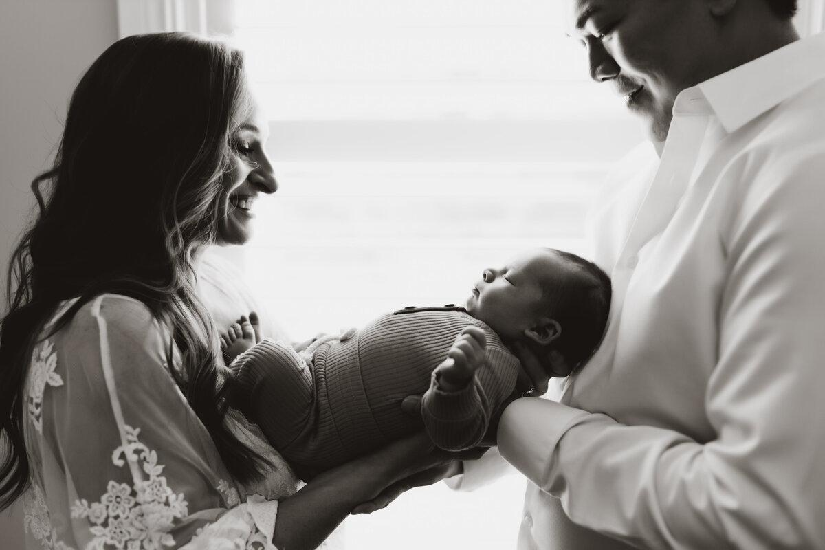 a black and white portrait of a mom and dad holding their sleeping baby at home