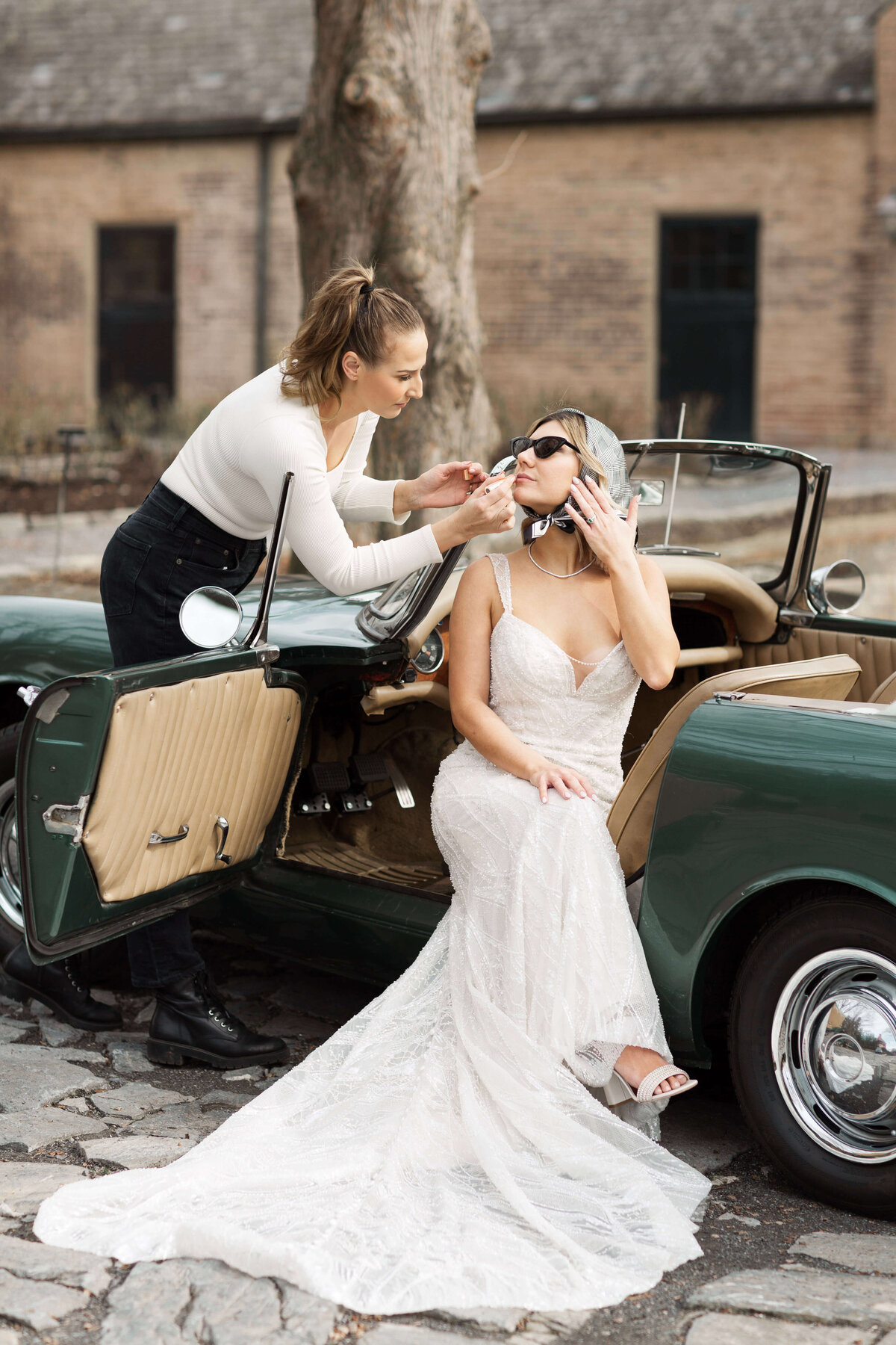 bride sitting in vintage convertible car getting her makeup touched up