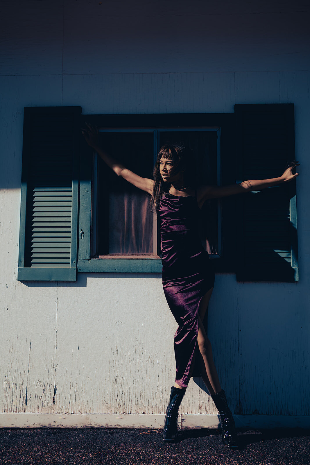 young black woman stands against wall and window outside facing toward the sun with arms outstretched