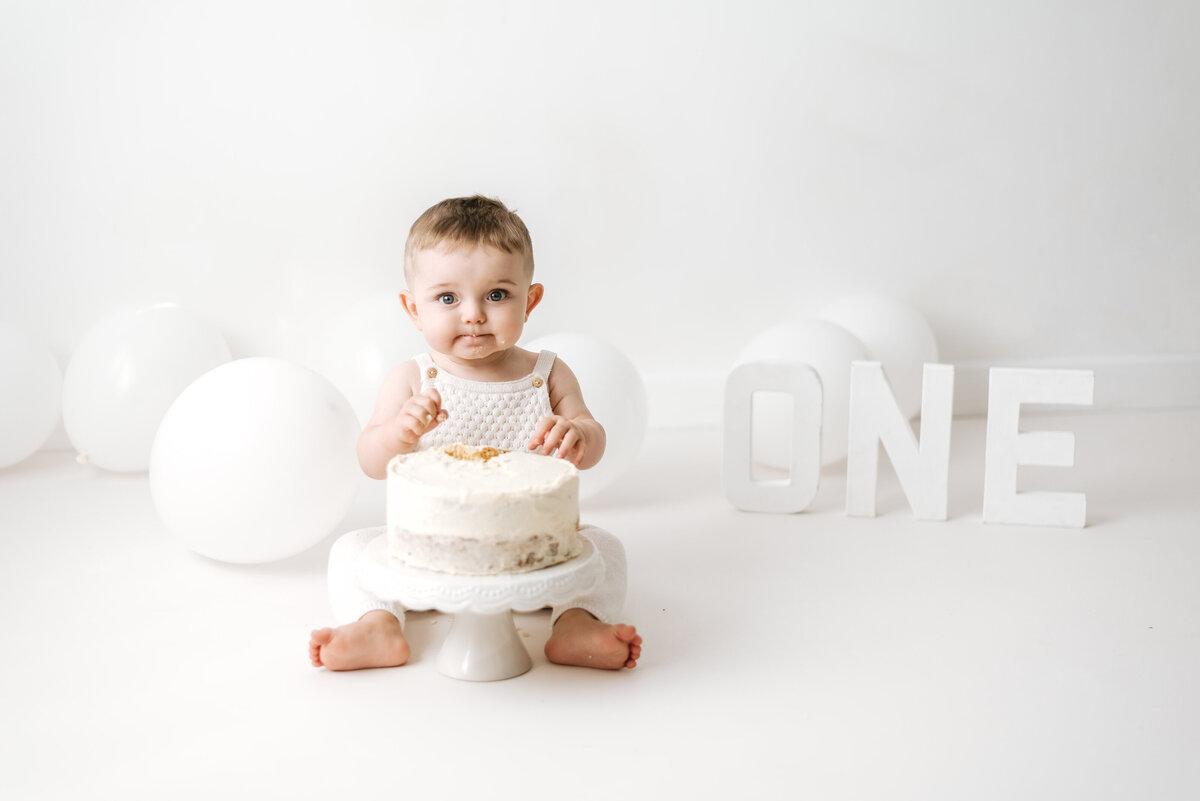 a one year old boy sitting with a cake at cake smash photoshoot in west sussex