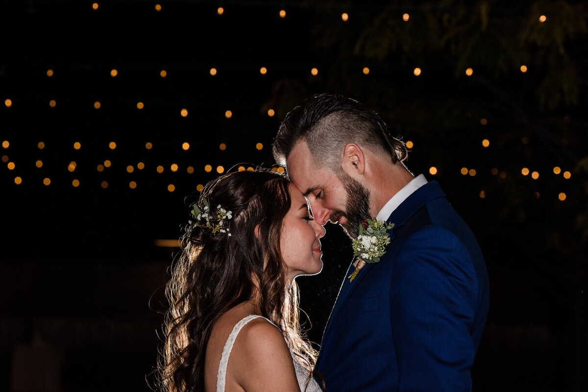 Bride and groom share a romantic moment at night in front of fairy lights
