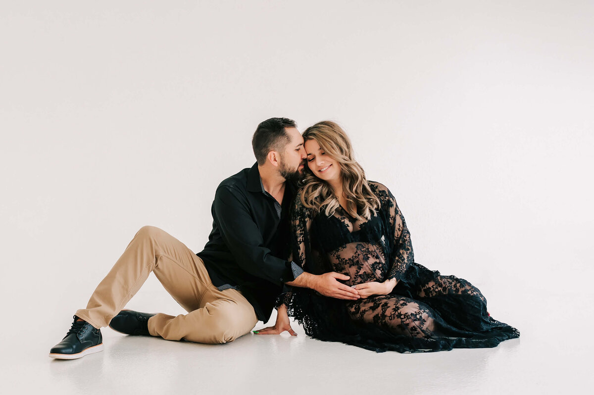 maternity photo of pregnant couple cuddling on floor in maternity photography studio in Joplin MO