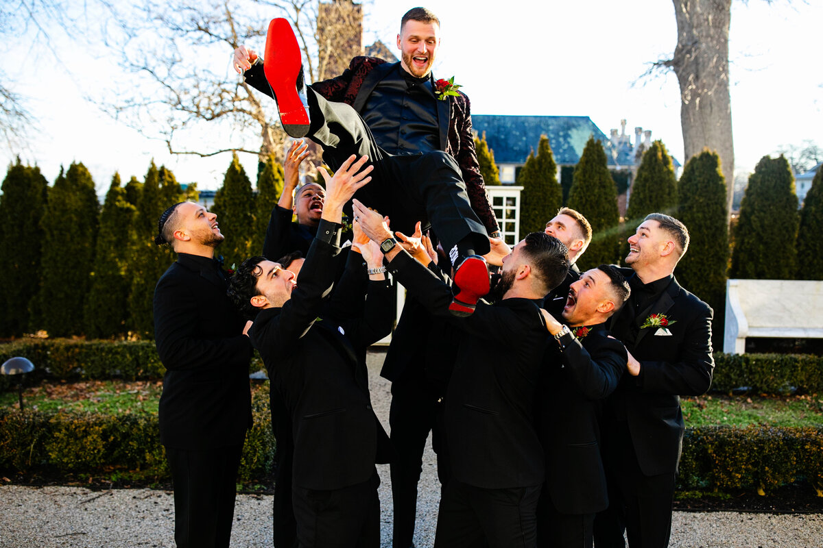 A groom in his Louis Vuitton shoes is thrown into the air by his groomsmen at Rosecliff Mansion.