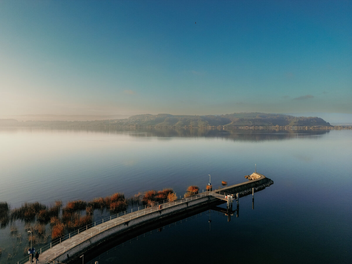 Drone picture of a lake in Switzerland in the sunset with a long footbrige.