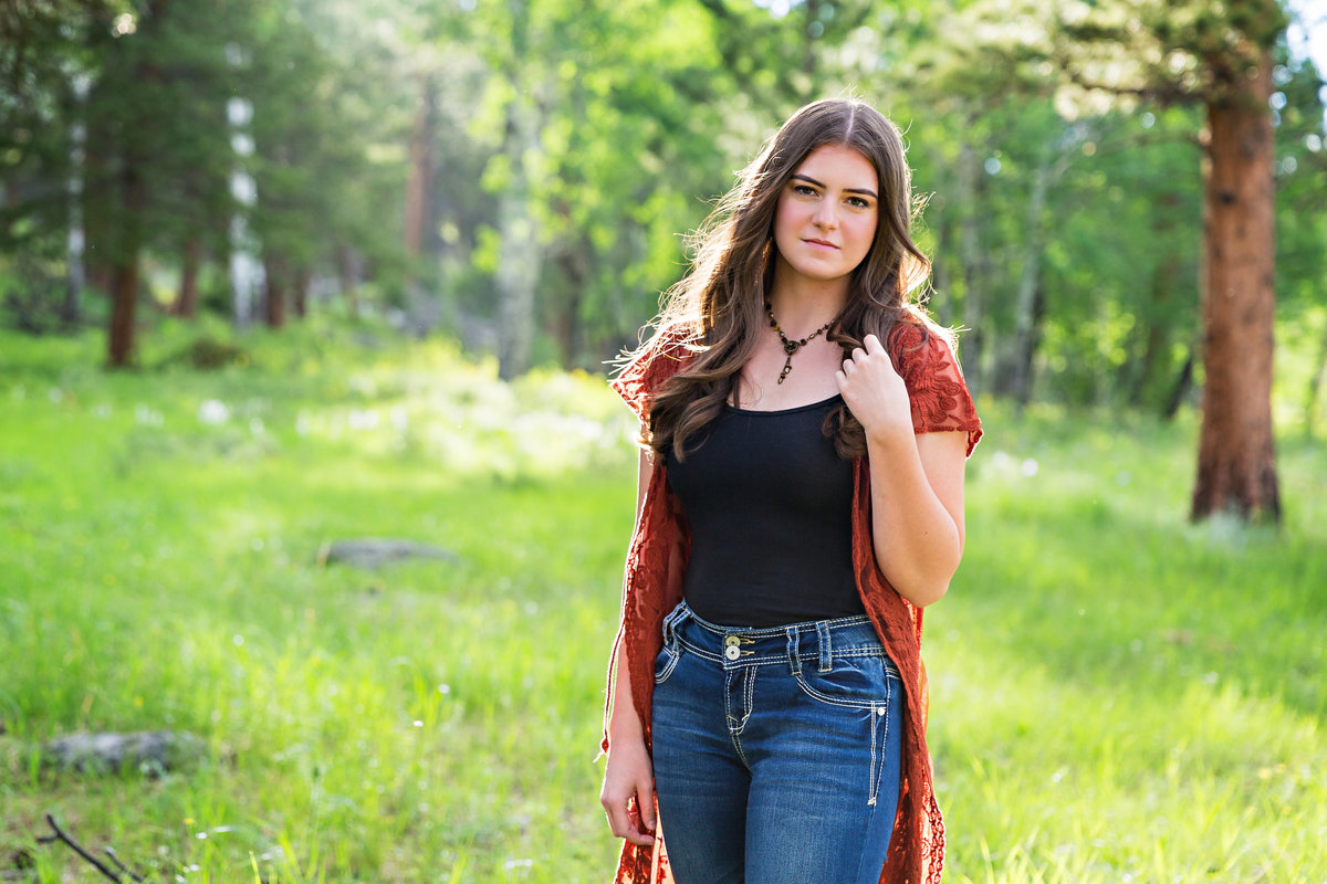 Serious teen girl poses for her senior photo session in a spring mountain meadow