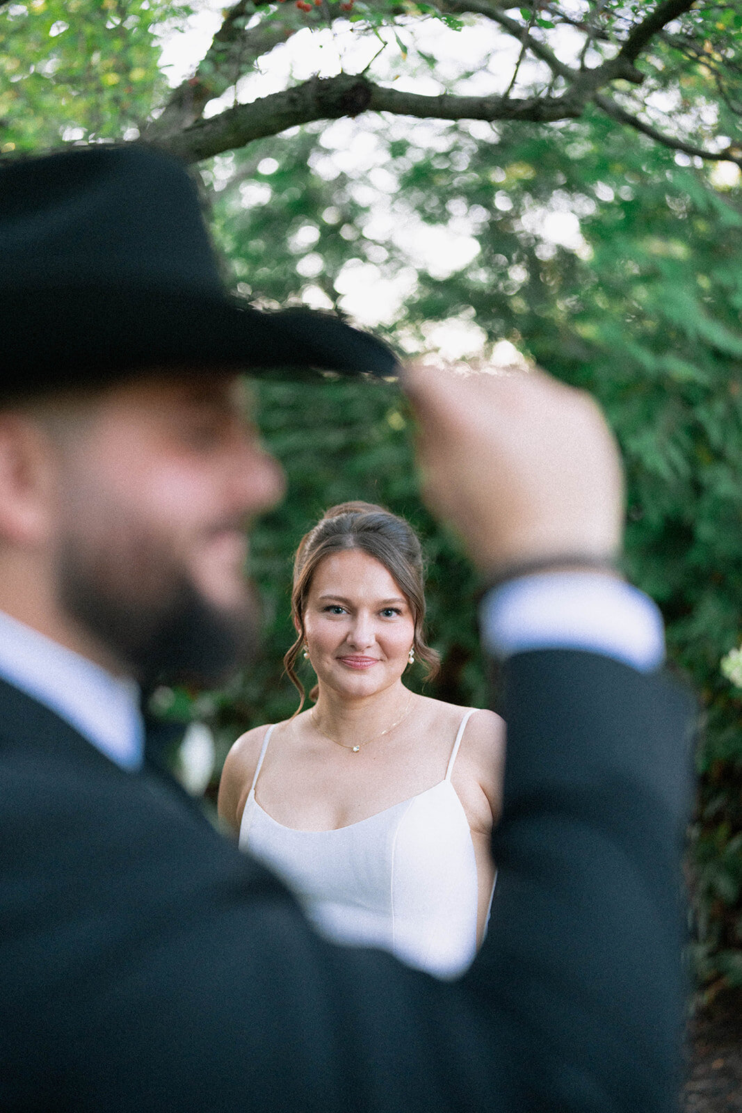 room tipping his black hat toward the bride during outdoor portraits at Café Cortina, romantic candid wedding photography.