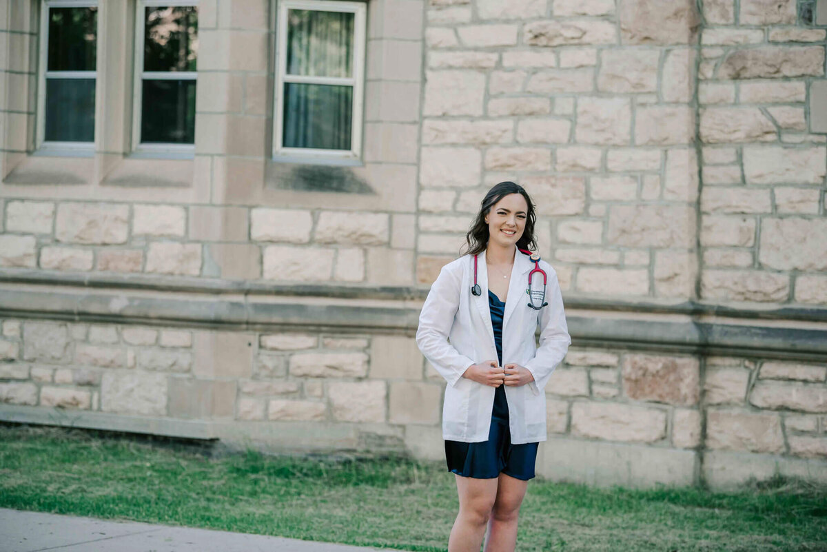 Wearing her white coat standing in front of a stone building. 