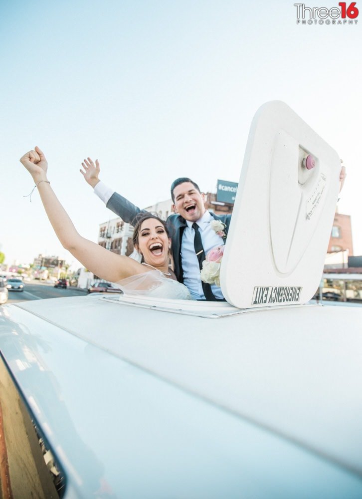 Bride and Groom poke their heads out of the of the limo and cheer as they are set to drive off
