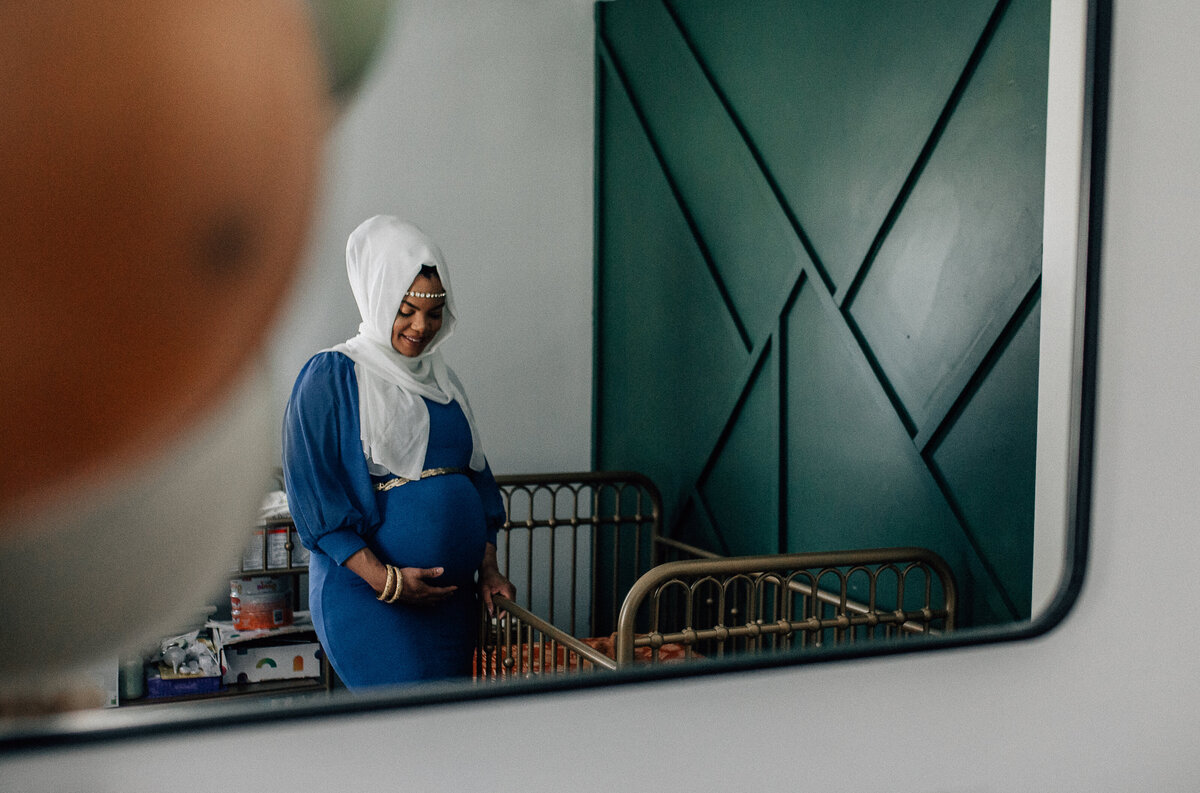 Maternity photoshoot with woman standing next to a crib.