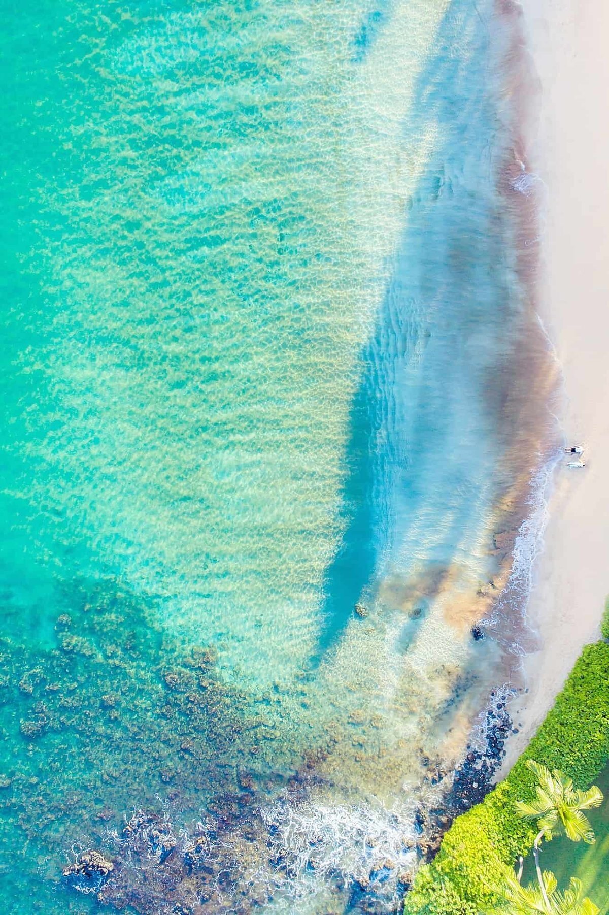 Drone image with couple featured on a white sand beach in Wailea surrounded by lava rock and turquoise ocean