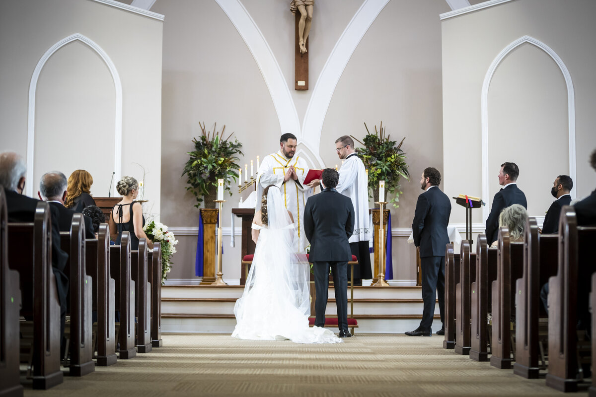 Bride and groom standing at the alter while priest officiates wedding.