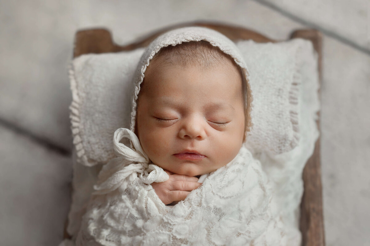 newborn baby girl with  bonnet and lace swaddle  in wooden bowl