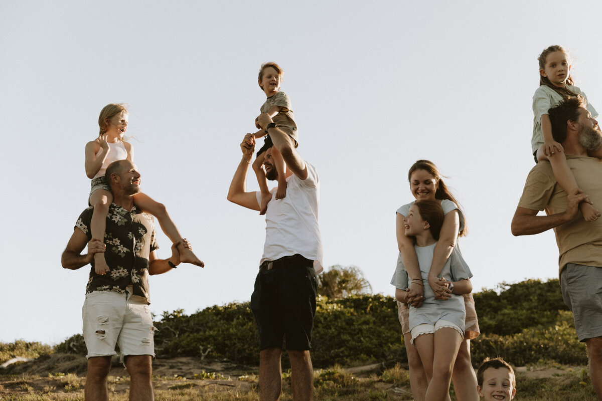 Big family together on the beach with their kids on their shoulders 