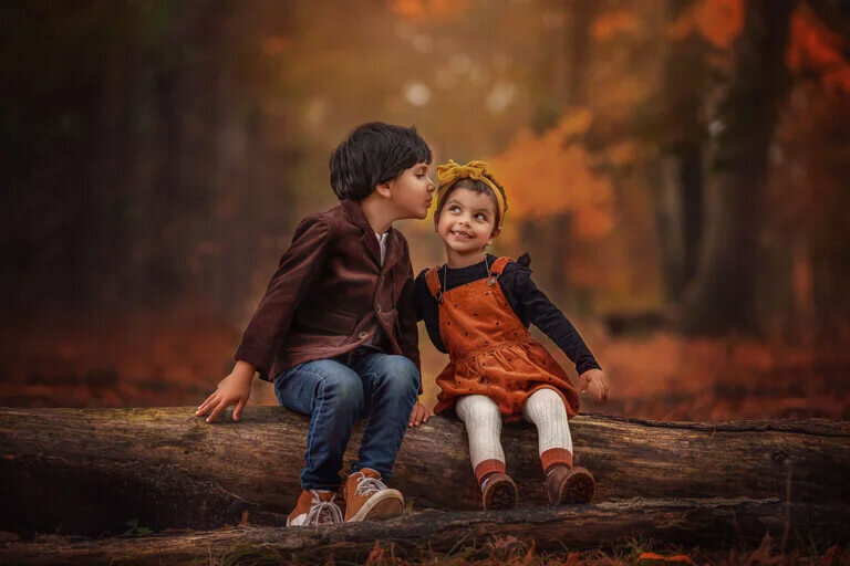 Siblings sitting on a long in the fall kissing on cheek