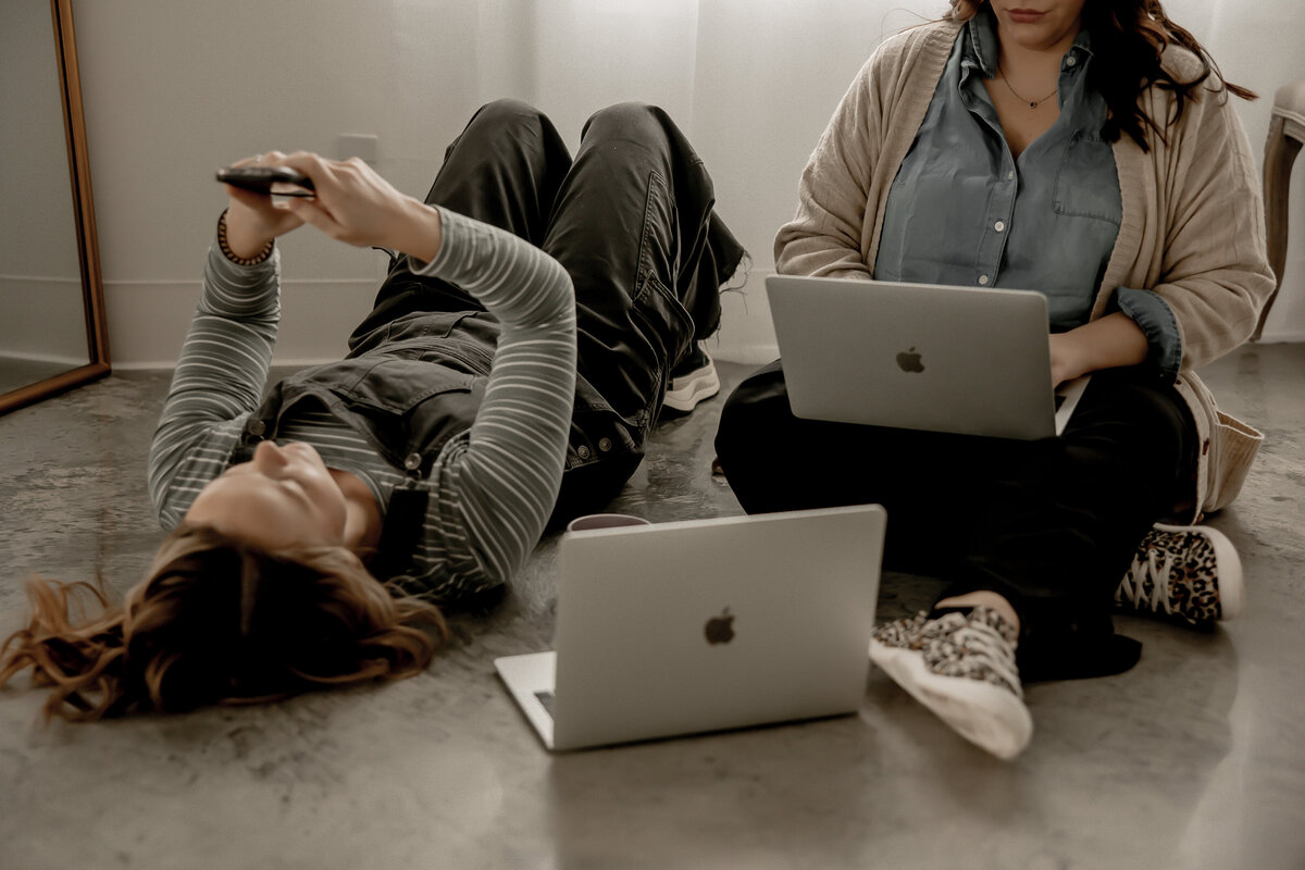 Amber laying on the floor with her phone up and Lacey working on her computer