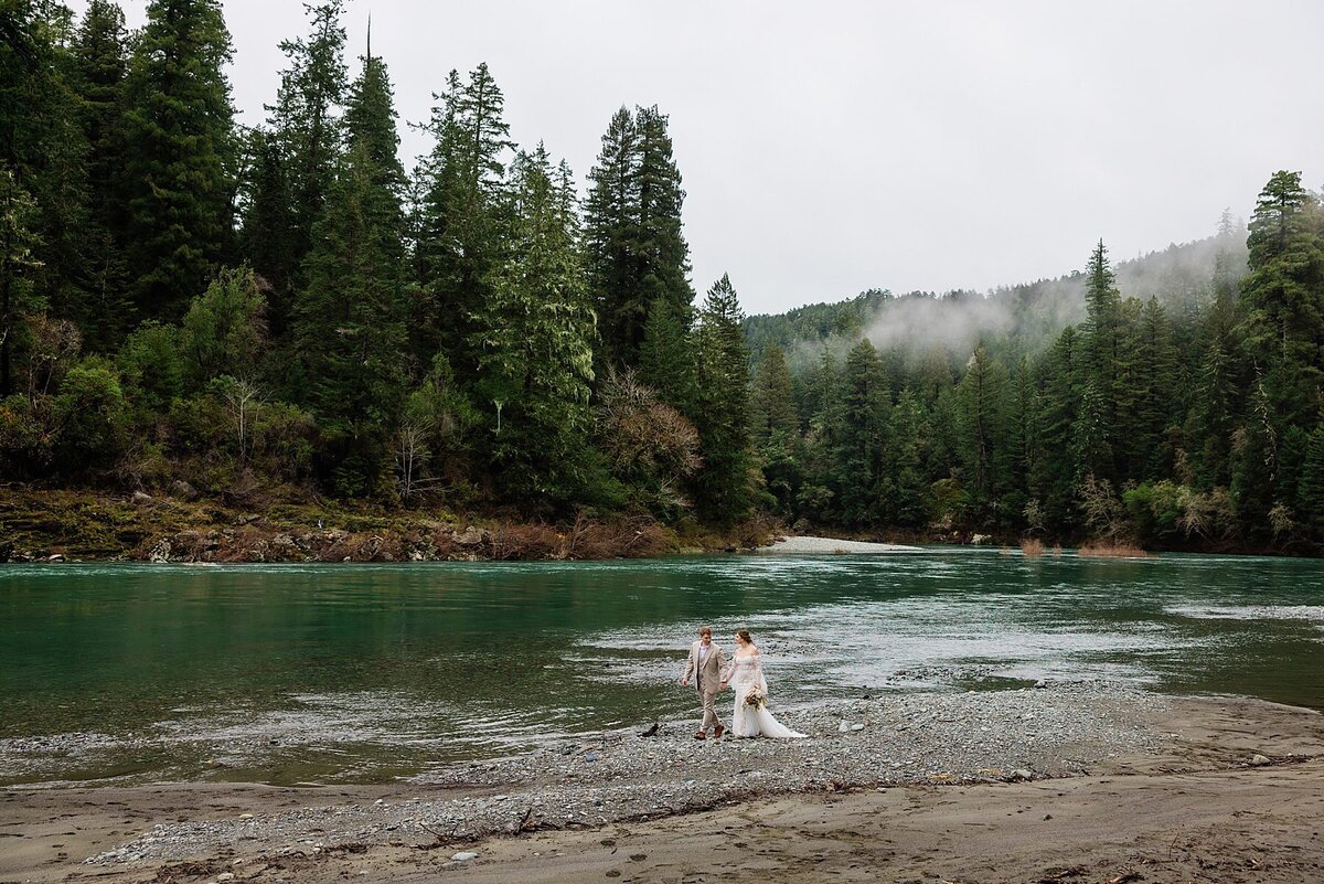 The bride and groom walk along the Smith River on their elopement day. 