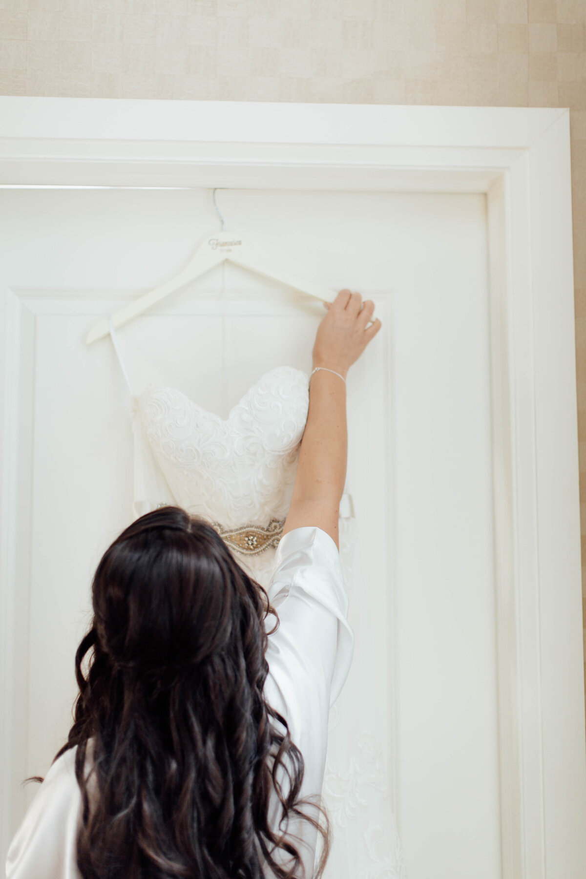 Bride grabbing dress from hook.