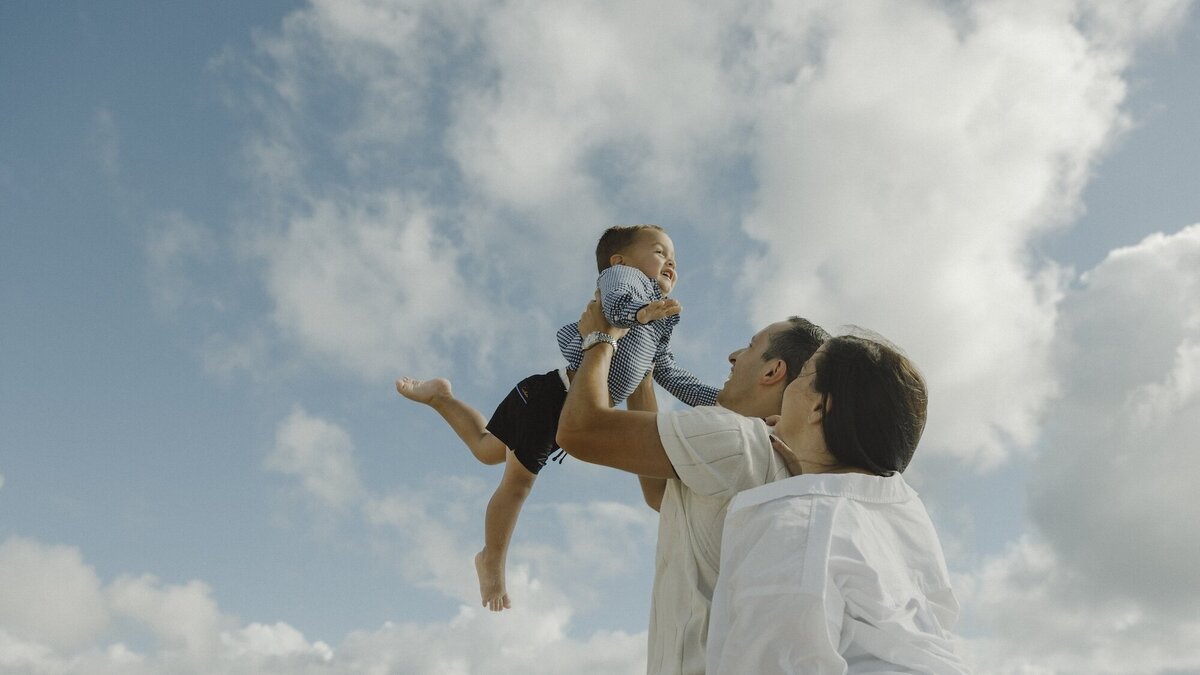 husband and wife play with their son on a beach in south florida