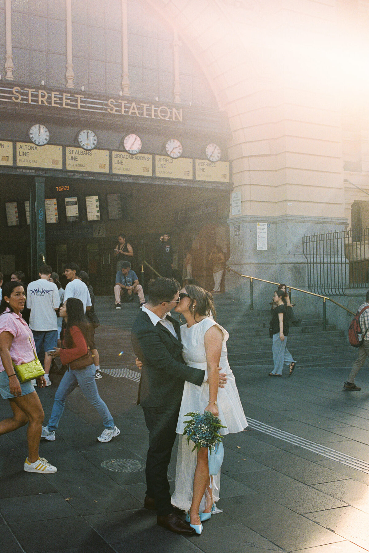 Couple standing in front of Flinders Street Station with crowds of people walking past, captured on 35mm film 