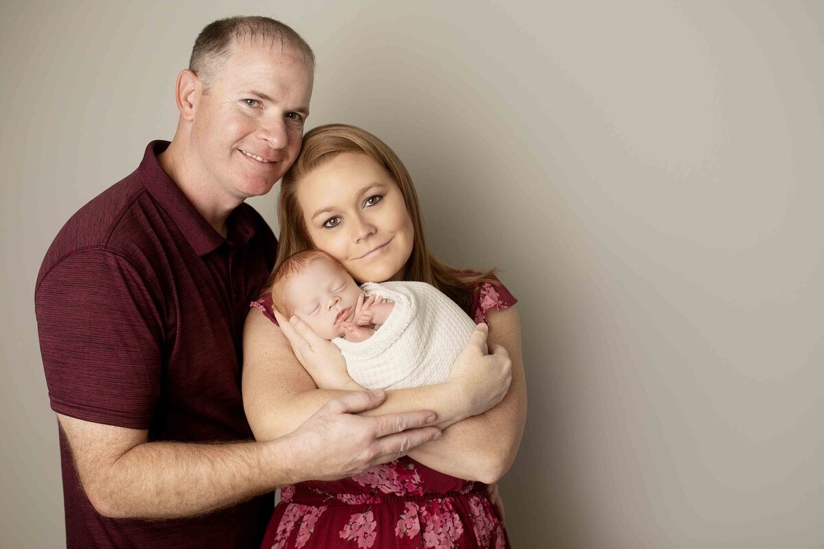 New parents cuddling their newborn in their arms, with soft smiles on their faces