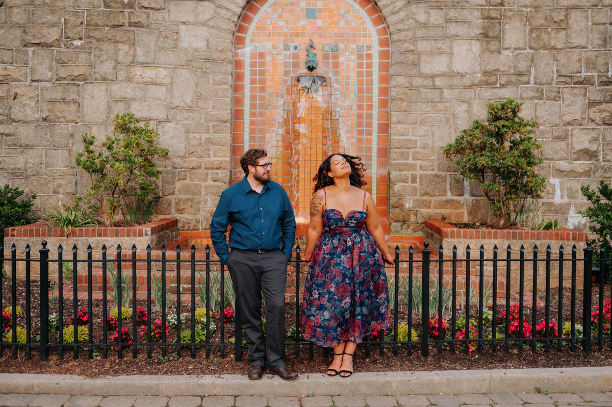 An engaged couple leans on a fence