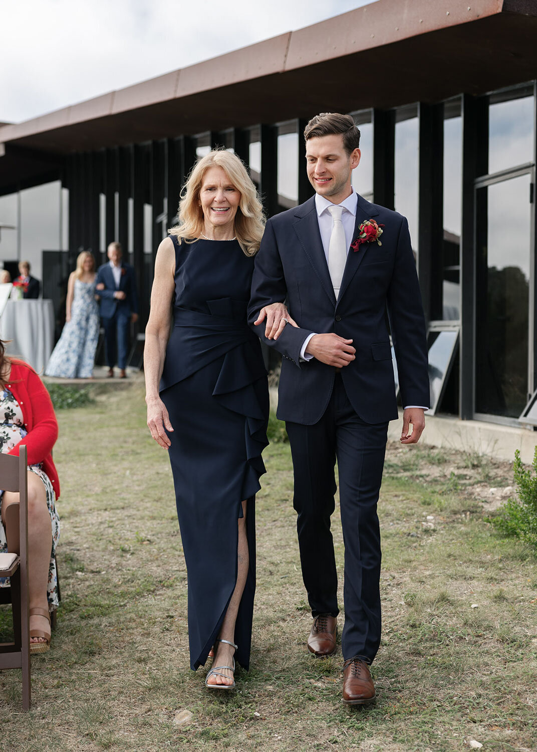Groom escorting his mother down the aisle in a navy suit