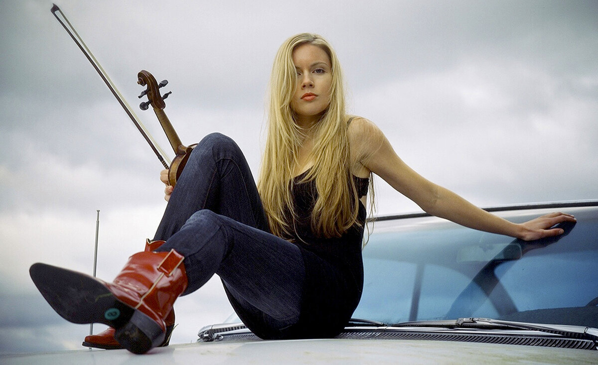 Country musician portrait Kendel Carson red cowboy boots blue jeans black tank top holding fiddle sitting against car windshield