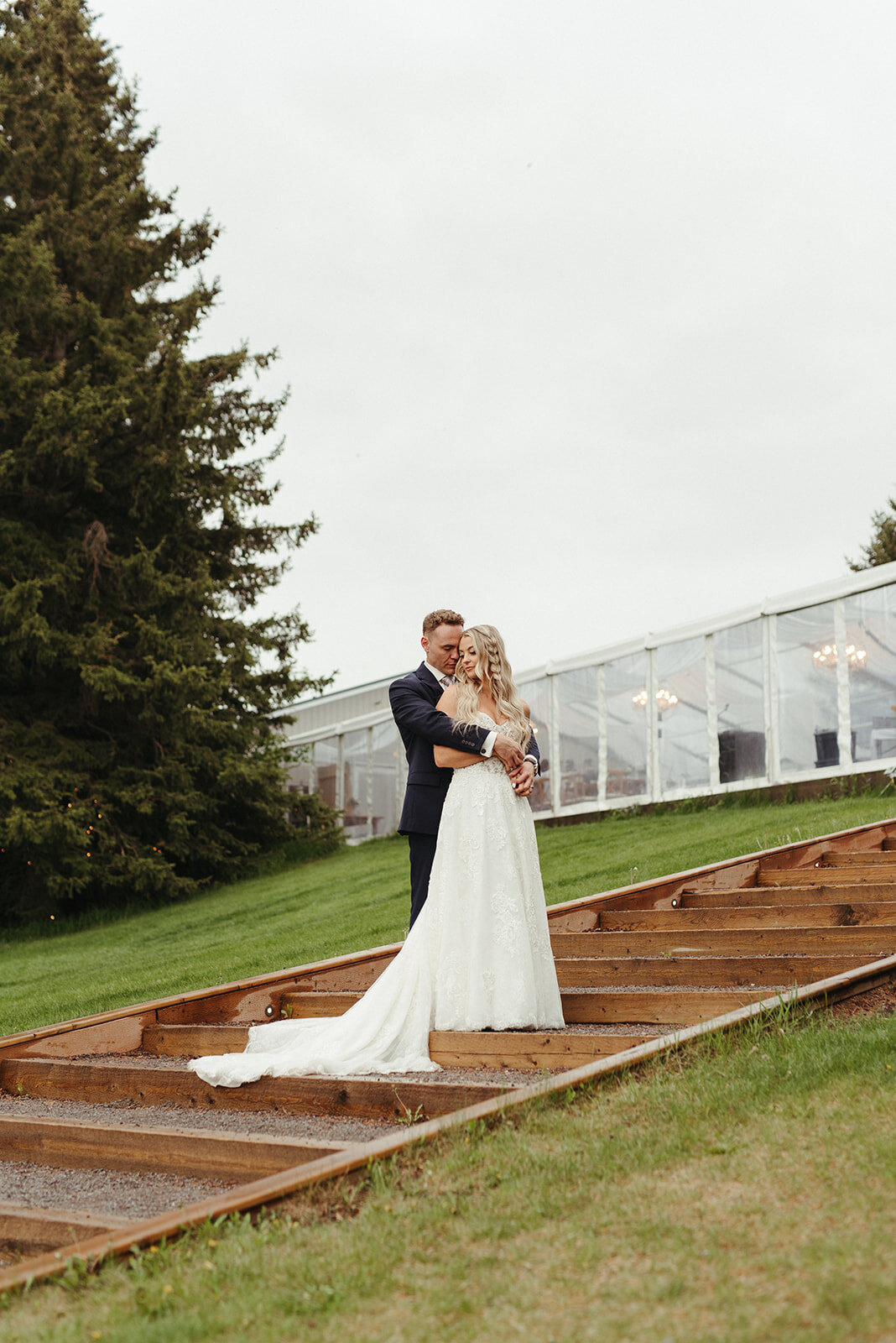 Bride and groom on the stairs at Pine & Pond, a natural picturesque wedding venue in Ponoka, AB, featured on the Brontë Bride Vendor Guide.