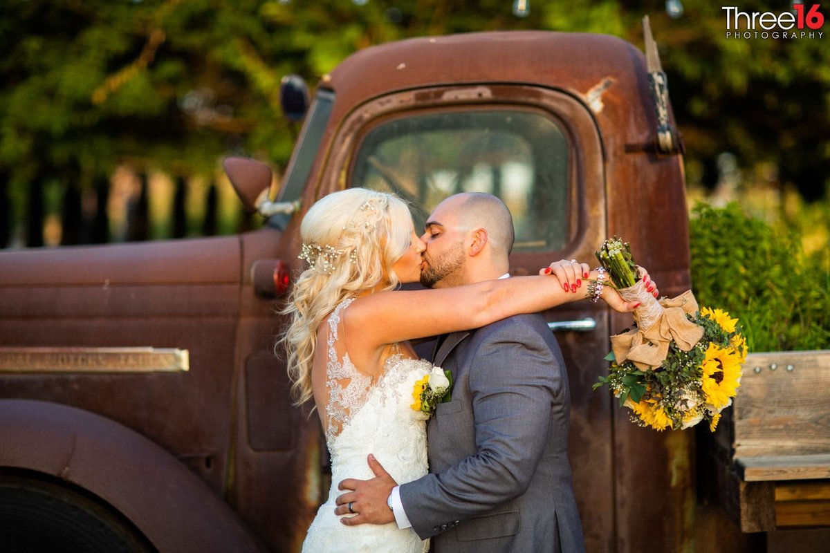 Bride and Groom share a kiss while standing in front of a rustic vintage truck