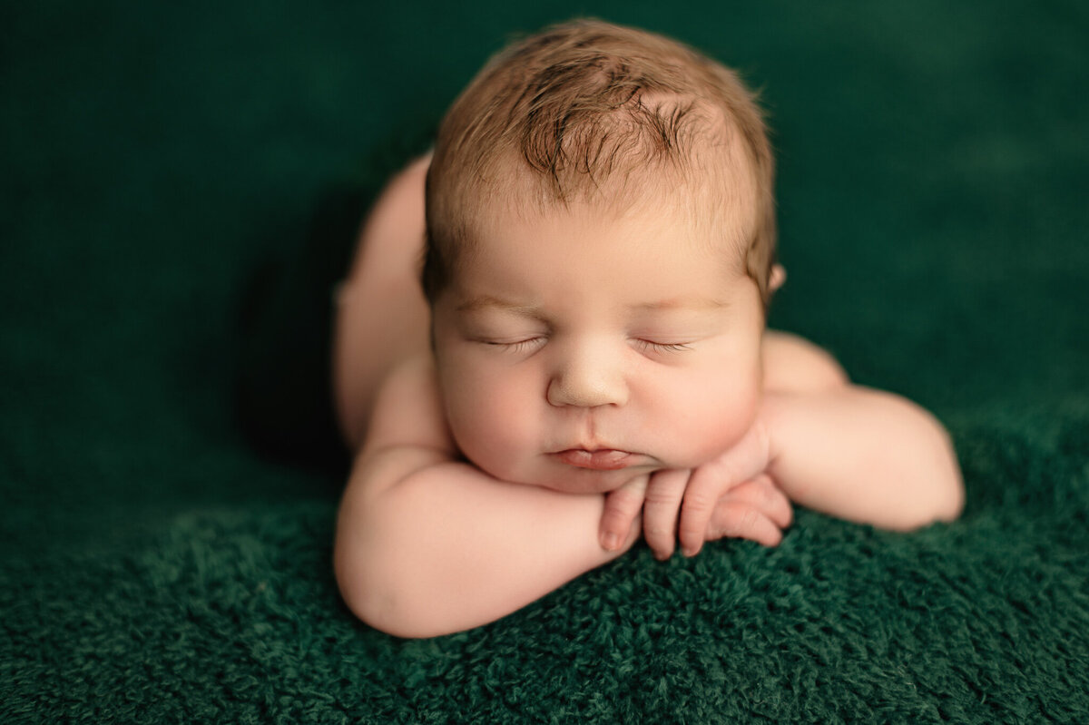 Baby boy sleeping on this hands on a green background.