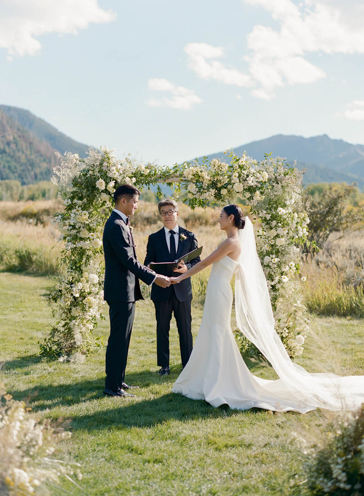 Bride and groom exchanging vows during their wedding ceremony at Aspen Meadows Resort, framed by beautiful mountain views and a lush, natural setting.