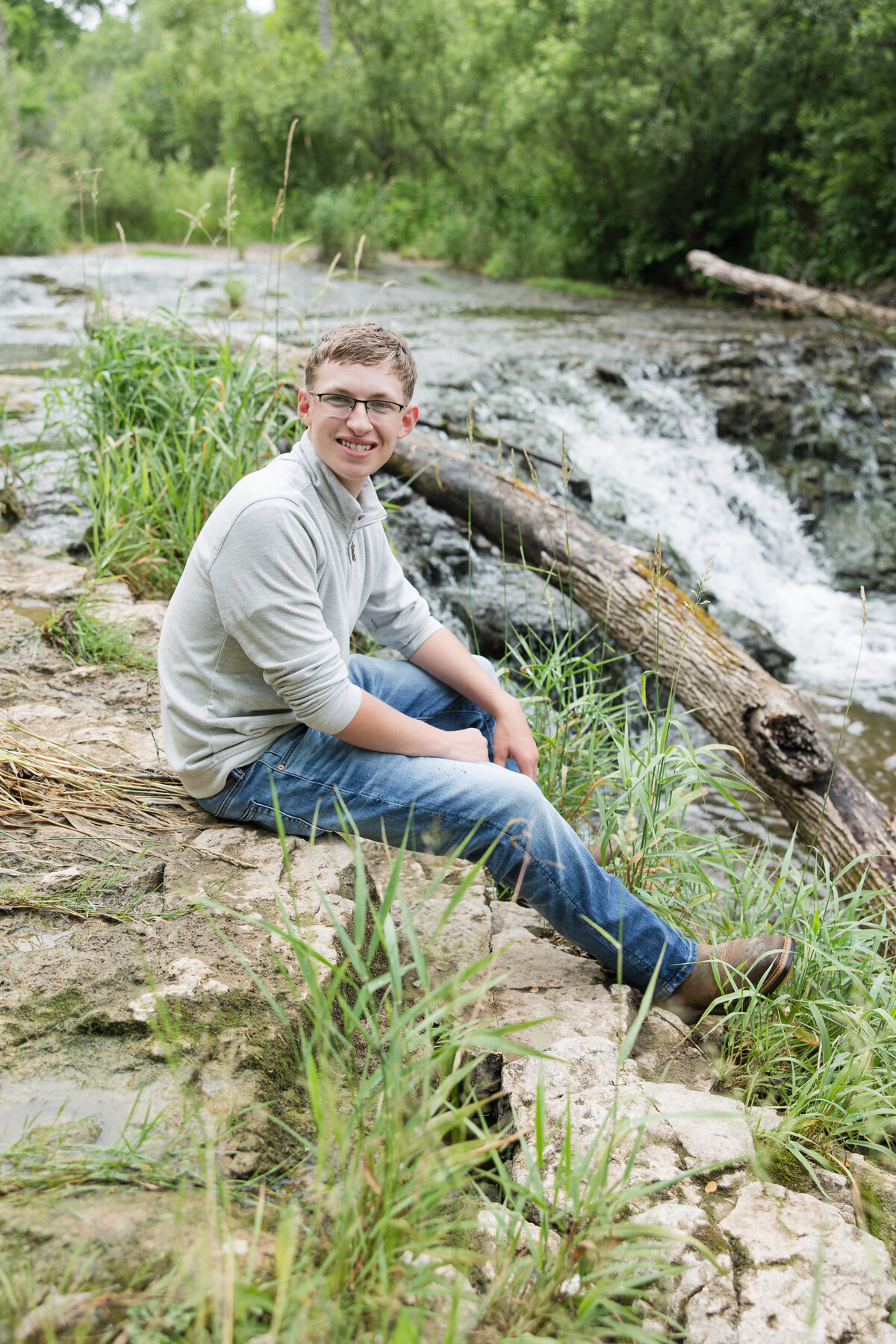 Senior guy seated on a rock ledge by a creek