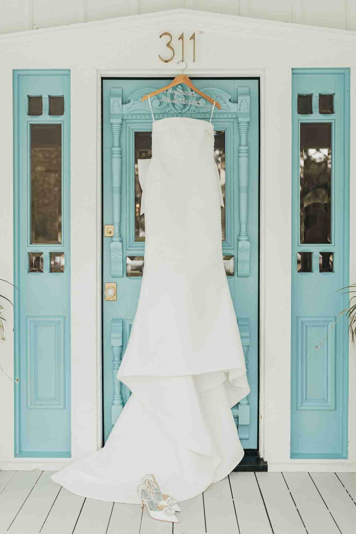 white wedding gown hanging on The Frenchie's turquoise door