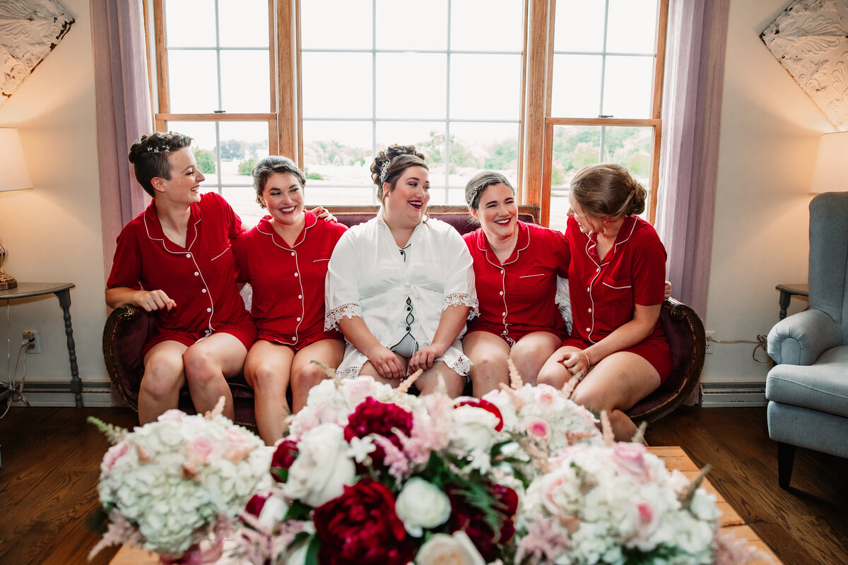 A bride sits on a bench laughing with her bridesmaids in pajamas