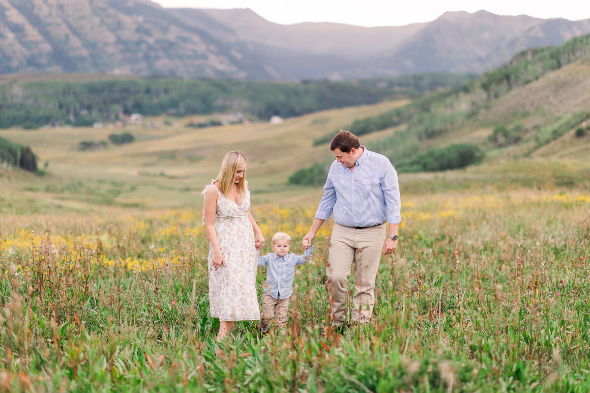 Photo of a mom and dad walking with their 3-year-old son in a wildflowers field at Mt Crested Butte, CO, capturing a joyful family moment