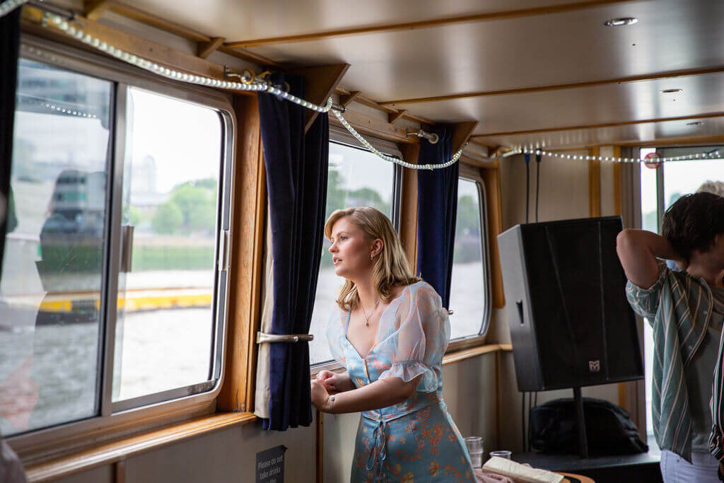 Female wedding guest staring out of window on London riverboat cruise
