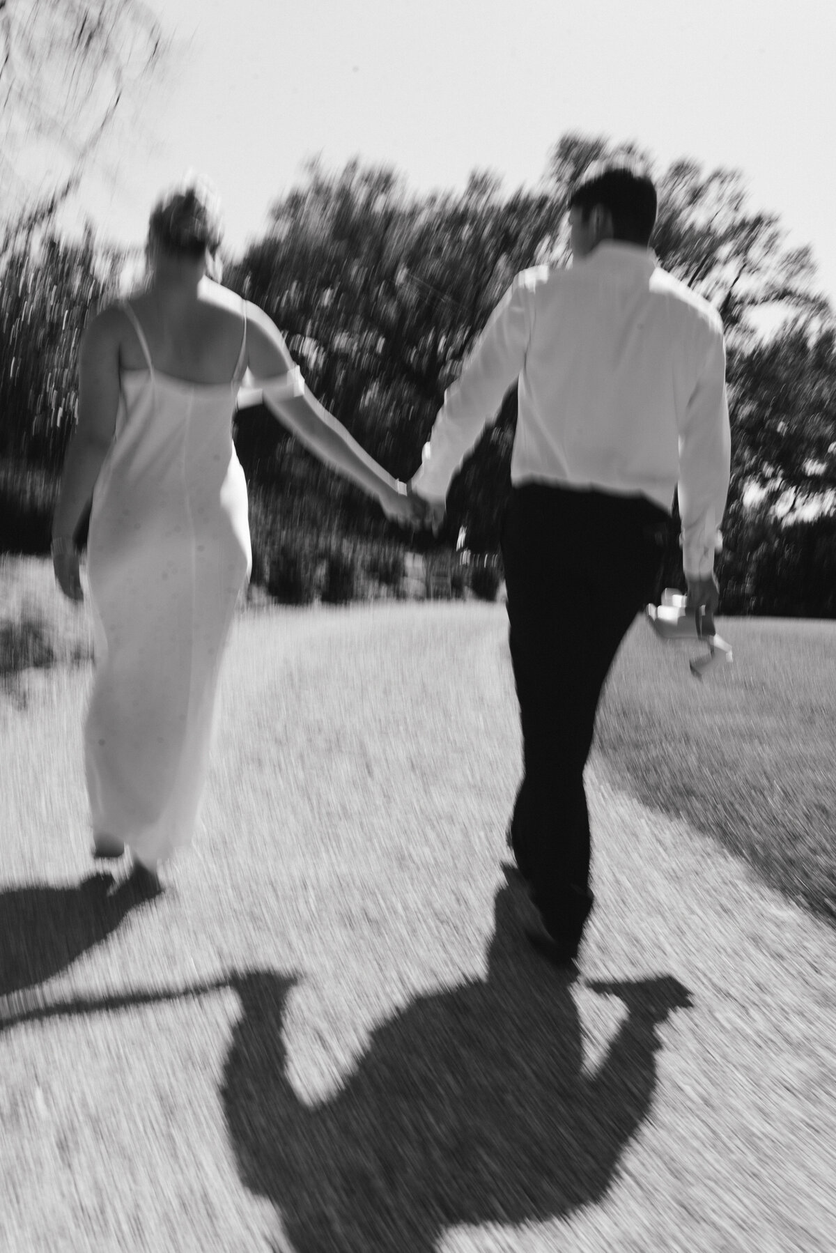 a black and white photo of a wedding couple walking while holding hands.