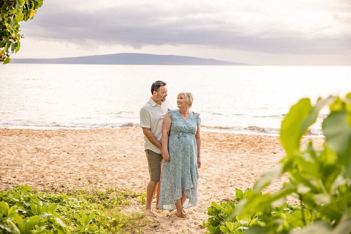 Maui Family Photographers capture woman holding man's hand while looking over shoulder on beach