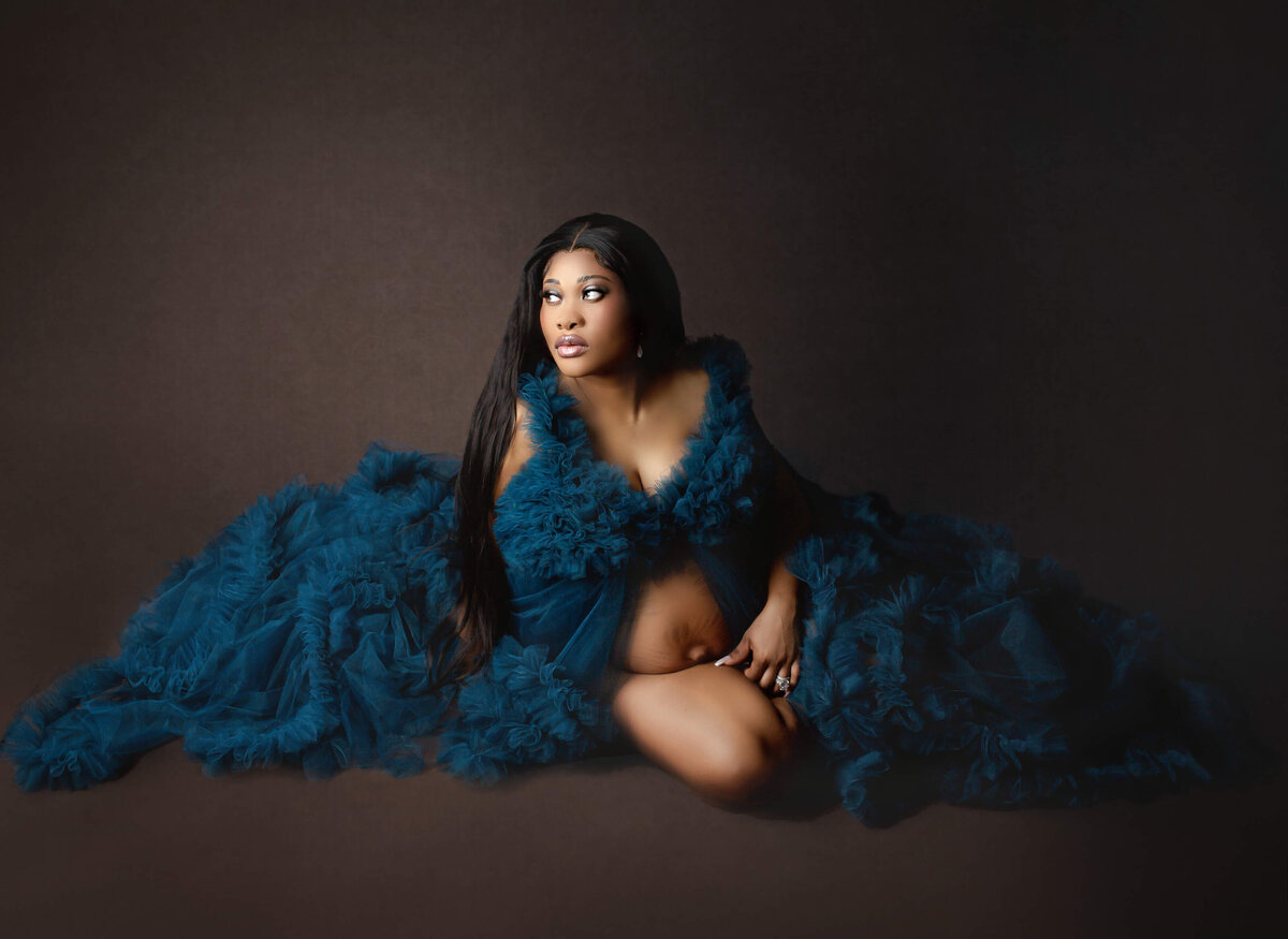 especting mother poses sitting, surrounded by blue tulle maternity gown at Hamilton, ON studio