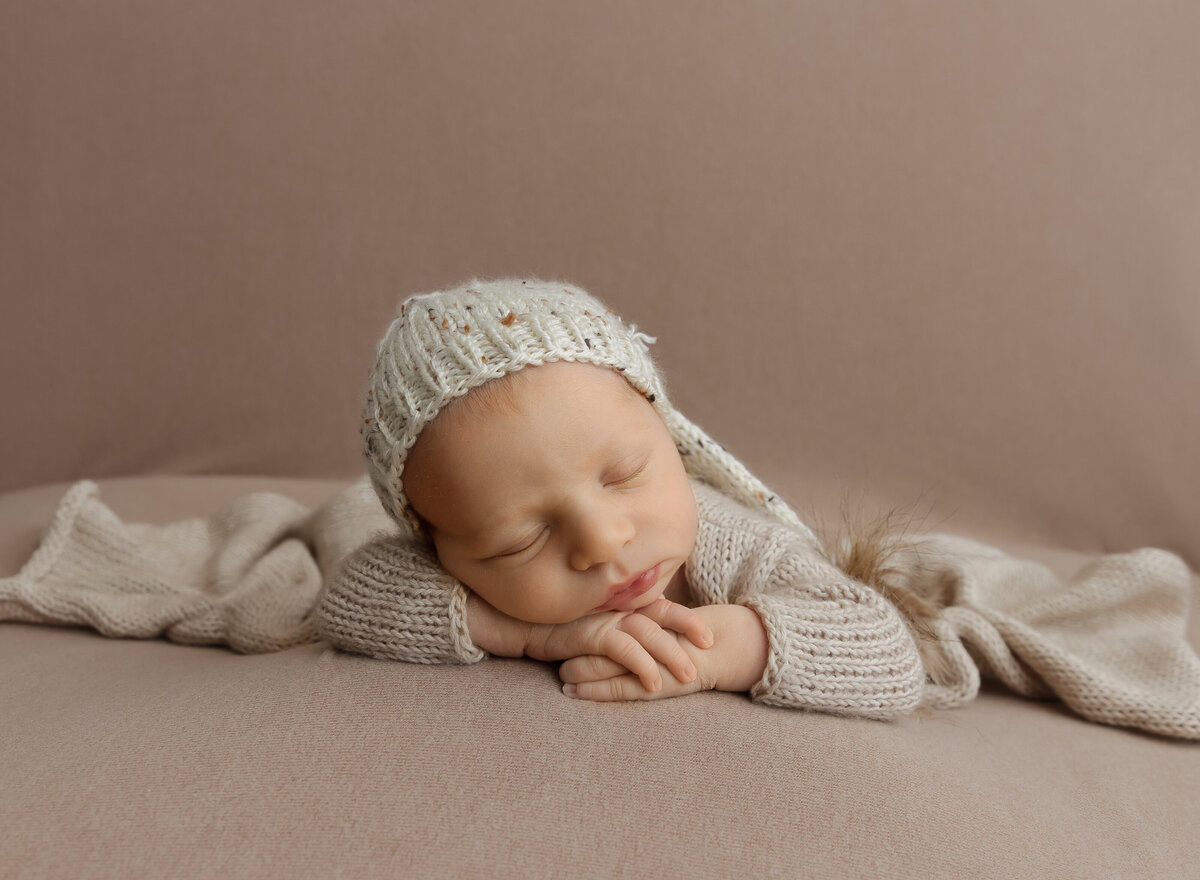Newborn photoshoot. Baby boy sleeping on his belly with his hands folded under his chin. Baby wearing a long cap. Captured by best Brooklyn, NY newborn photographer Chaya Bornstein.