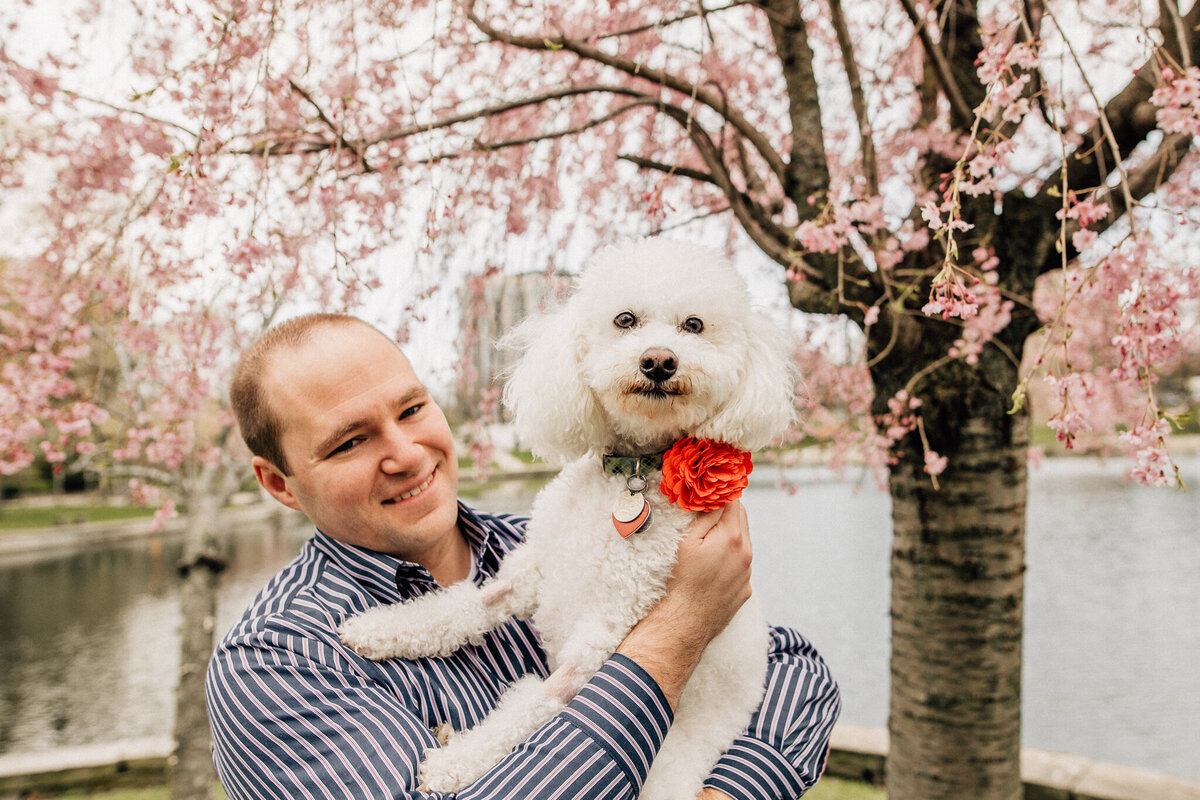 Man holds with poodle dog outside.