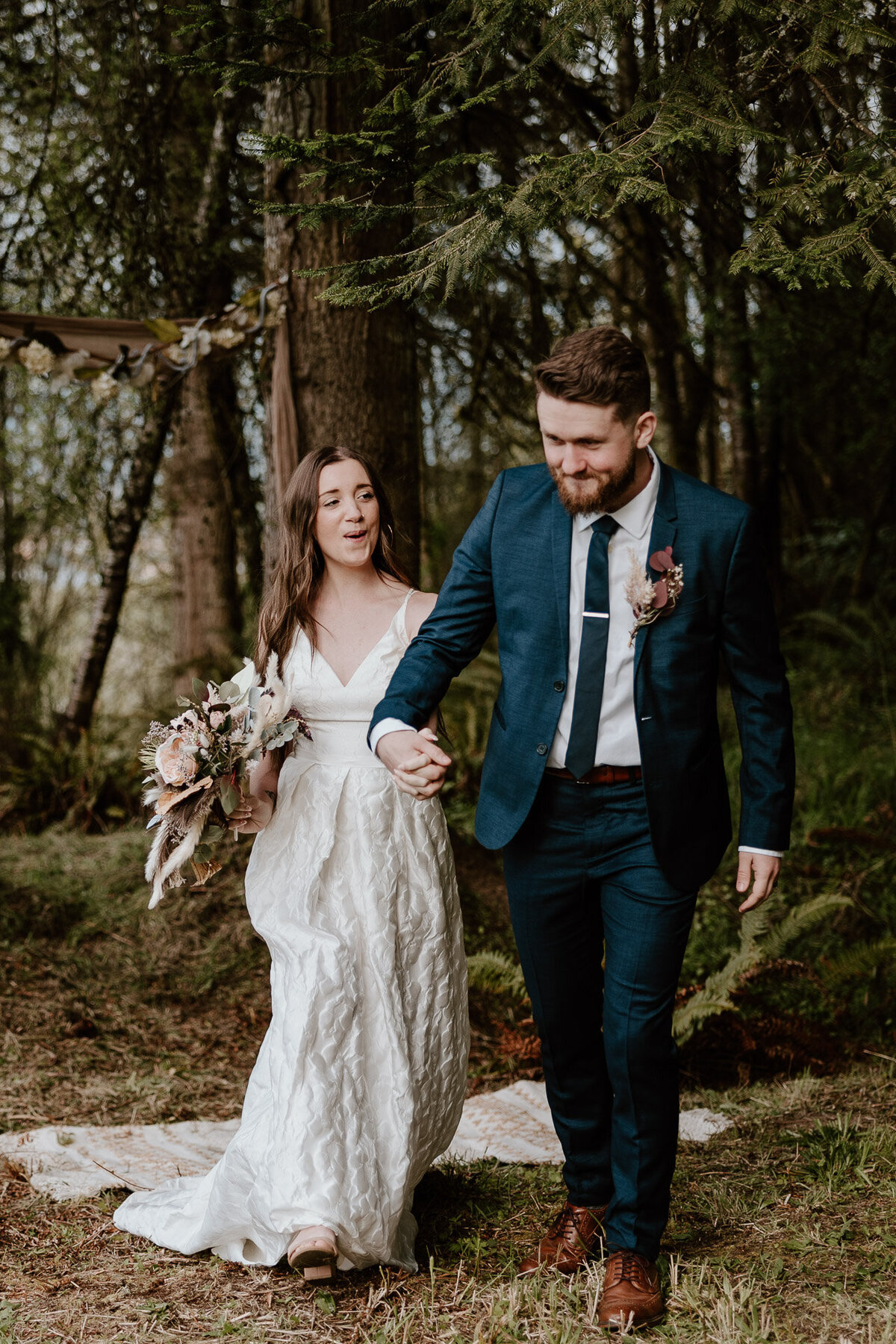 A moment captured by a Hood River Wedding Photographer of newlyweds laughing and hiking through a forest while holding hands