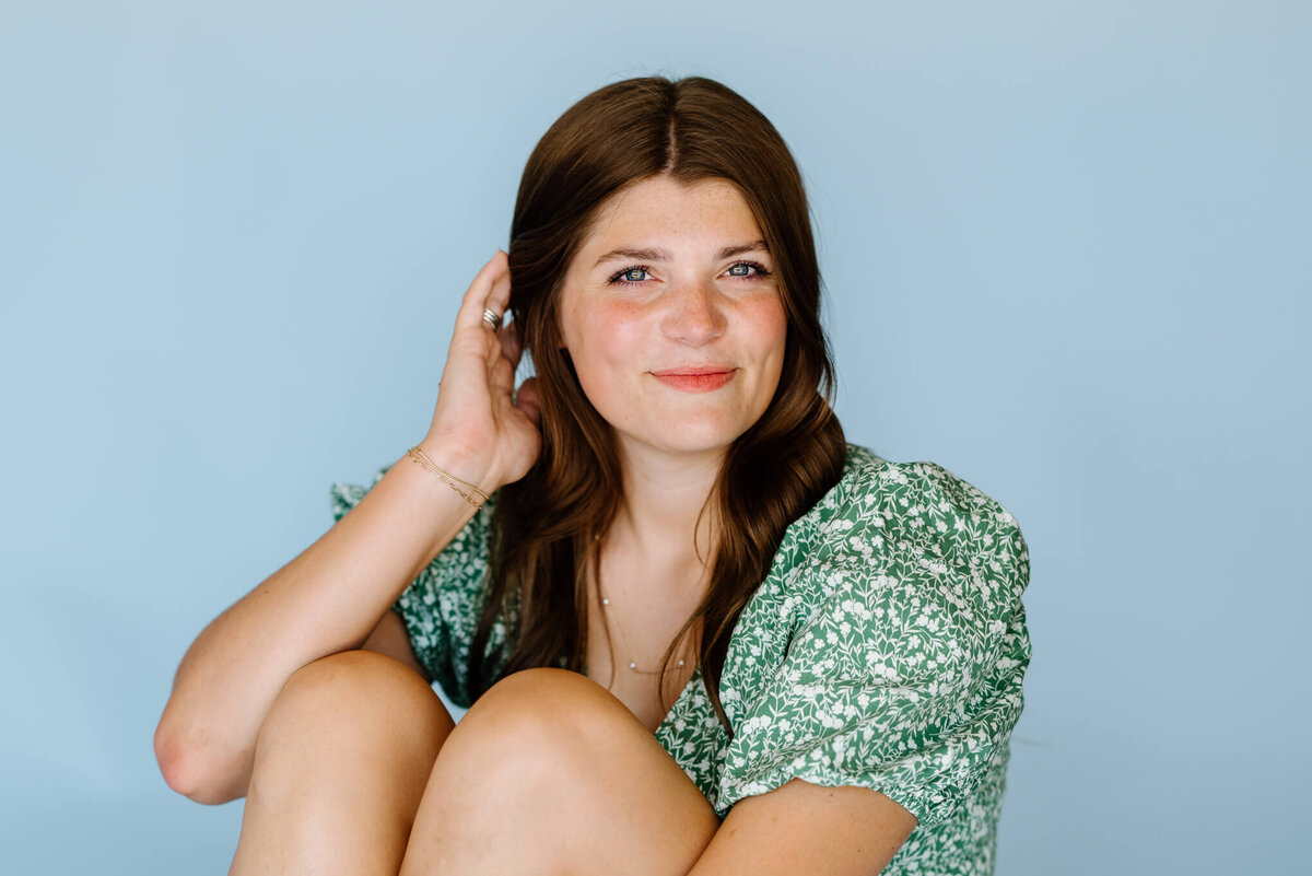 headshots of Marshall, TX graduate in green floral ruffle top sitting in front of light blue backgroun