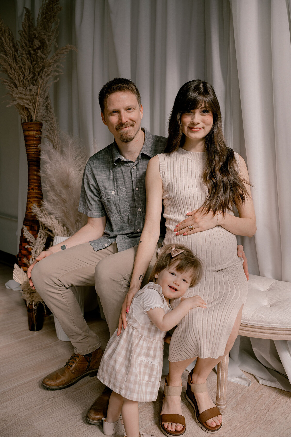 Two parents with a small child in front of them while one rest their hand on their baby bump