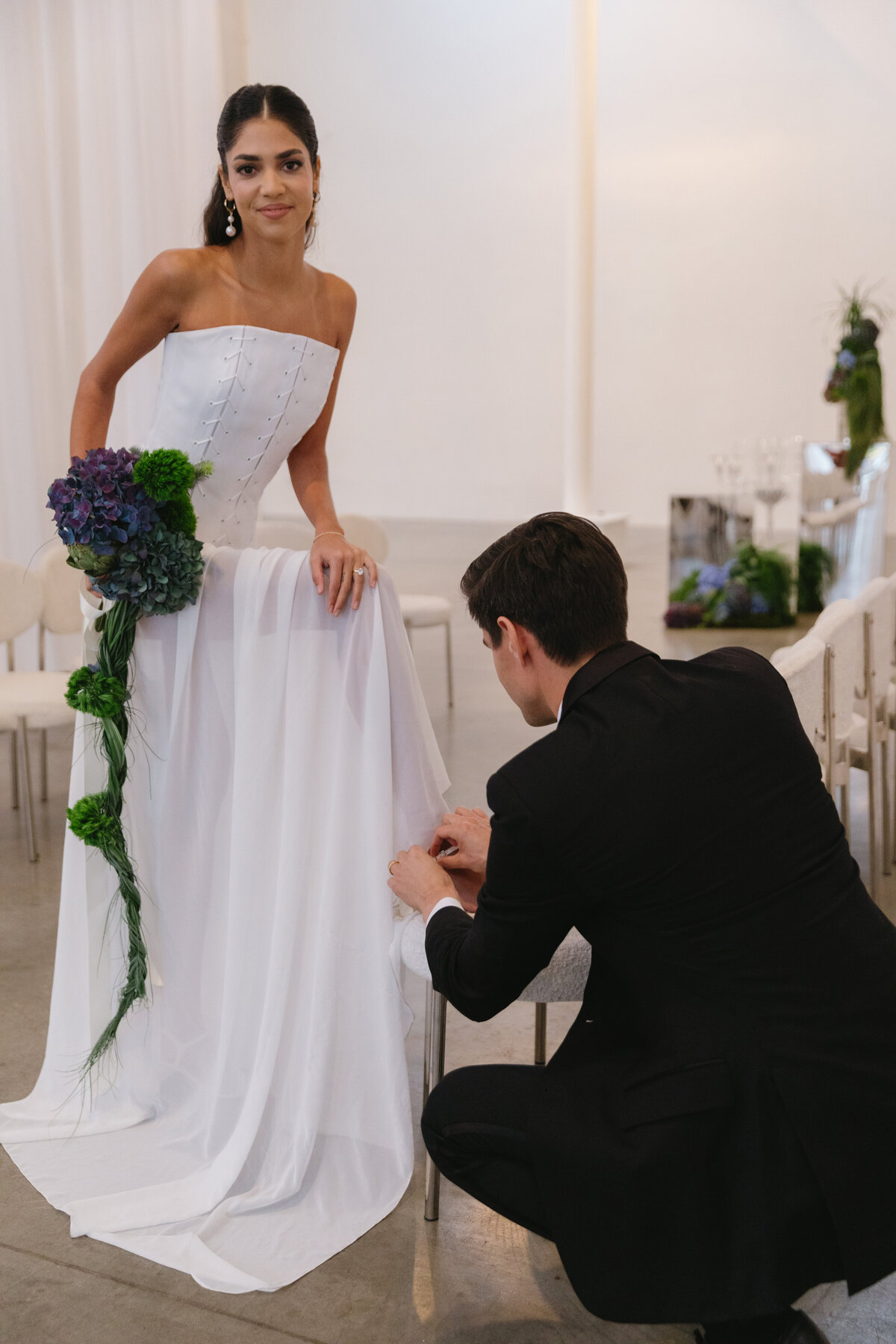 Romantic wedding detail of groom kneeling to adjust the bride’s gown.
