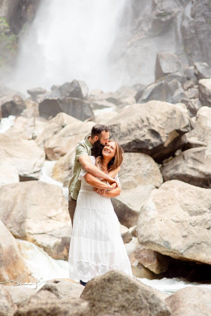 Woman laughs as her fiancé hugs her from behind during their engagement session at Yosemite.
