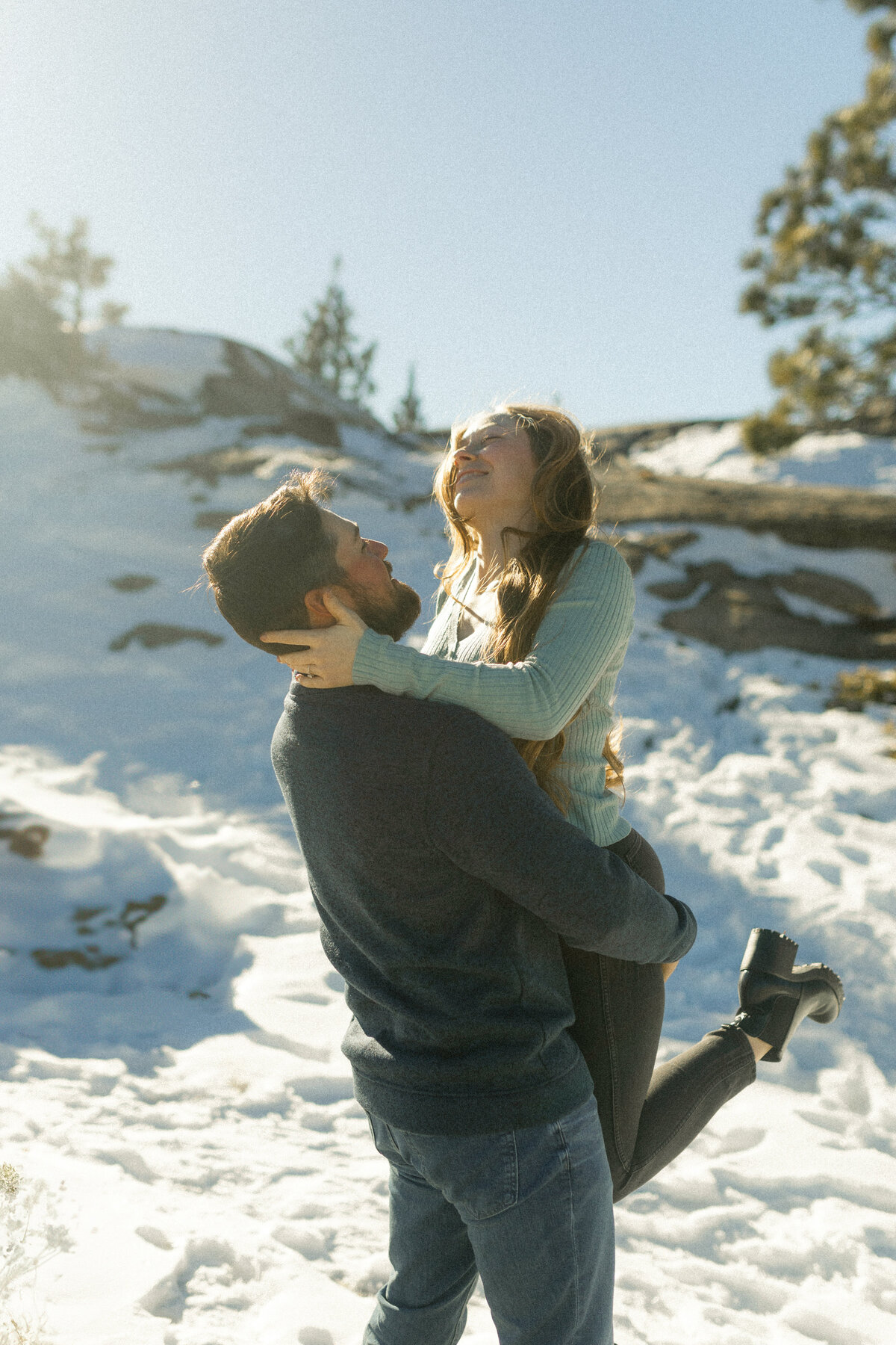 Guy picking up girl in snow during winter engagement session in mountains